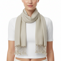 A woman wearing a light beige scarf with fringed tassels, styled over a white short-sleeve crop top against a plain white background.