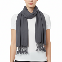 A model wearing a dark gray scarf with fringed tassels, styled over a white t-shirt against a plain white background.