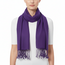 A model wearing a solid purple knit scarf with fringe tassels, styled around the neck over a white t-shirt against a plain white background.