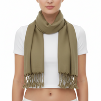 A woman wearing a light olive green scarf with fringed tassels, styled over a white crop top against a solid white background.