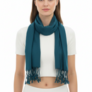 A woman wearing a teal blue scarf with fringe details, styled over a white ribbed short-sleeve crop top against a plain white background.