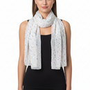 A woman wearing a lightweight white scarf with a scattered multicolor dot pattern, styled over a black sleeveless top against a plain white background.