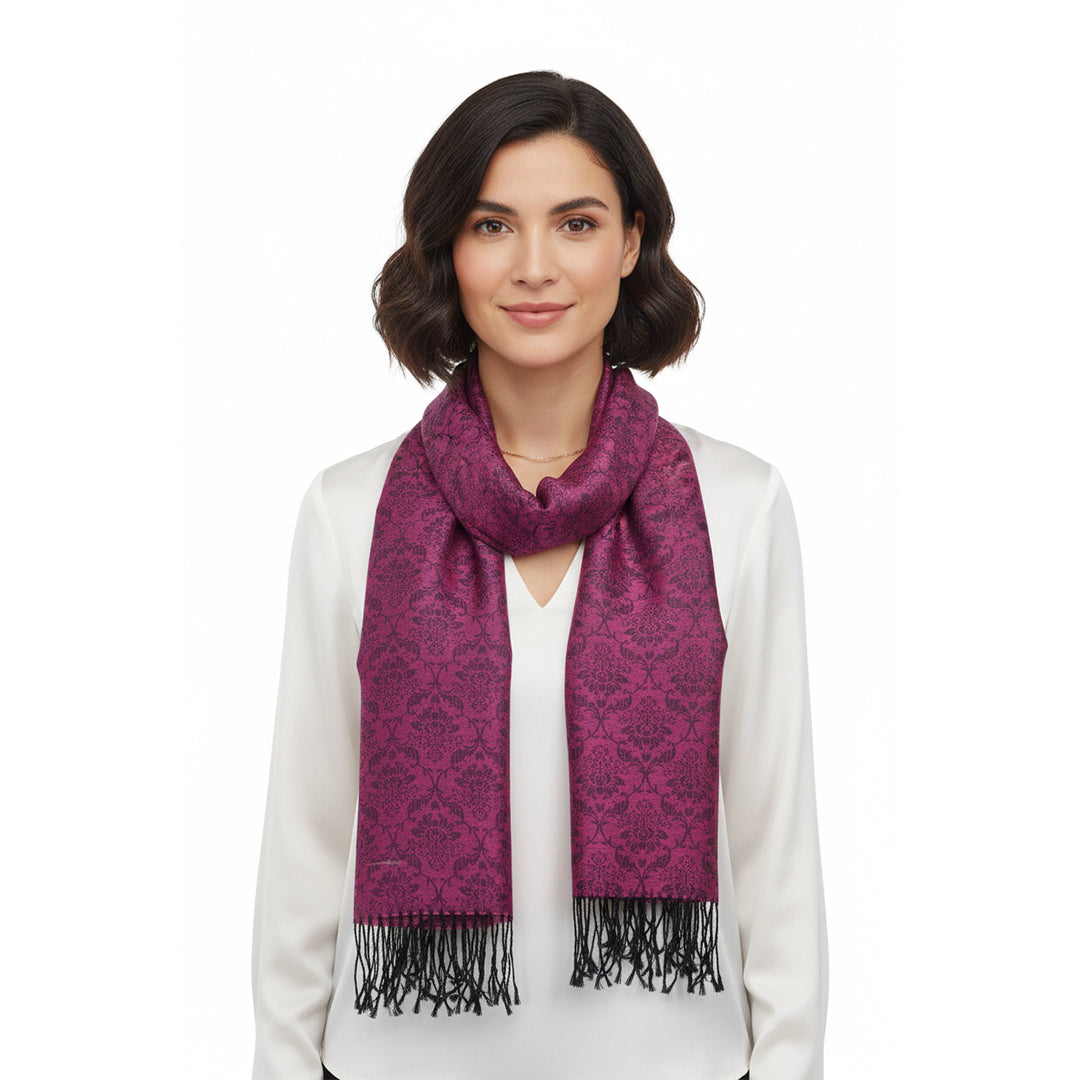 A woman with short dark hair wearing a white top and a magenta-purple patterned scarf with black fringe, photographed against a plain white background.