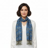 A woman with short dark hair wearing a blue patterned scarf with fringe, styled over a white top and blazer against a plain white background.
