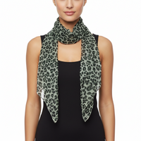A woman wearing a lightweight leopard-print scarf in sage green and black over a black sleeveless top, photographed against a plain white studio background.