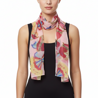 A model wearing a lightweight pink scarf with a colorful butterfly and floral print, styled over a black sleeveless top against a plain white background.