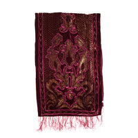 A rectangular burgundy velvet prayer rug with intricate gold and magenta embroidery, featuring a central floral motif and fringed edges, shown against a plain white background.