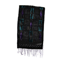 A black woven textile with geometric and diamond patterns in purple and teal, finished with fringed edges, shown against a plain white background.