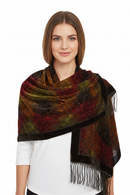 A woman modeling a large patterned shawl wrap with fringe, shown against a plain white studio background. The wrap has a dark base with a mottled abstract pattern in red, brown, gold, and olive green, plus black border and fringe.