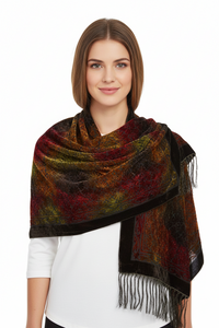 A woman modeling a large patterned shawl wrap with fringe, shown against a plain white studio background. The wrap has a dark base with a mottled abstract pattern in red, brown, gold, and olive green, plus black border and fringe.